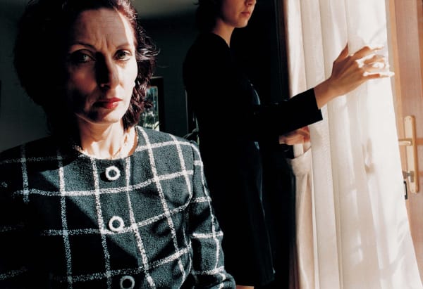 Elinor Carucci Mother is mad woman's angry face in shadow while another woman pulls back a curtain in the background