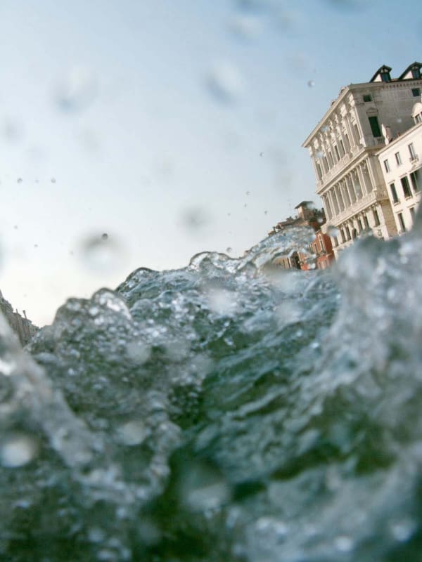 water and splashes on bottom half of the frame, three buildings (2 white + 1 red) on top right side, from Venezia series, by Mona Kuhn