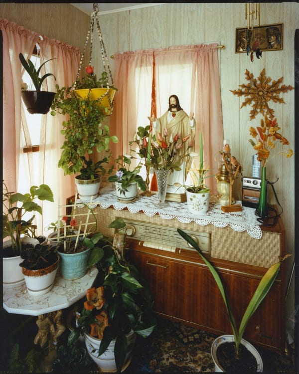 Bruce Wrighton Jesus statue on top of stereo console, plants on console, table, and floor, in front of corner windows Tirage C-print d'époque 20 x 25 cm Dim. papier: 20 x 25 cm