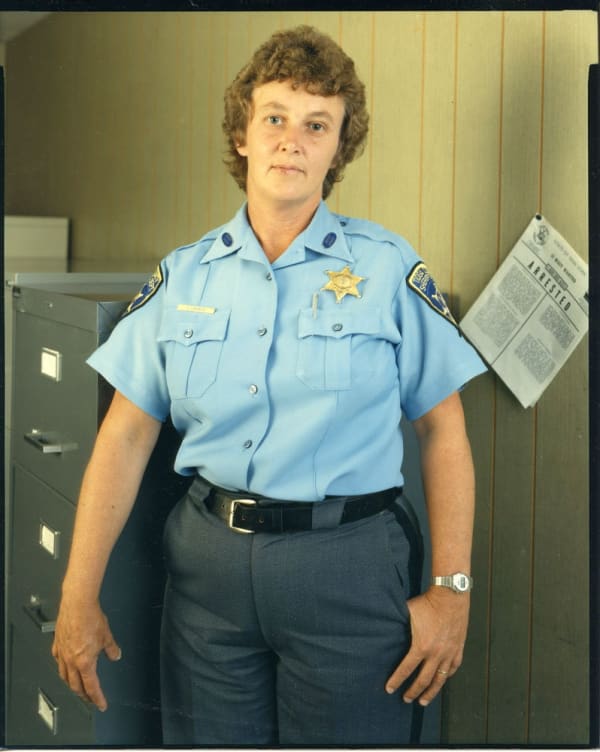 Bruce Wrighton Woman in blue Tioga County Sheriff uniform, with file cabinet on left and ARRESTED noticed on right Tirage C-print d'époque 20 x 25 cm Dim. papier: 20 x 25 cm