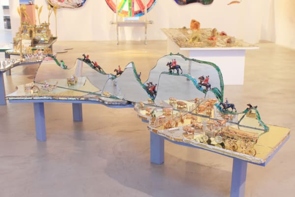 Mixed media sculpture by Andrew Logan, combining mirrored or reflective fragments, coloured materials, and found objects in a playful, textured vertical form. vocative of youthful memory and play.