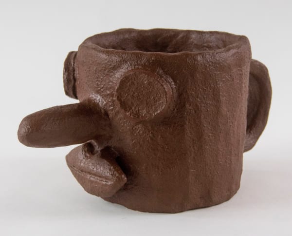 A sculpture of a mug featuring a face with a long nose by artist Reniel Del Rosario