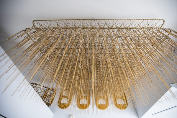Installation shot of a golden metal spring mattress with golden metal tassels hanging from it.