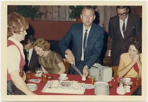 ENLARGEMENT REPRINT Vernacular, Untitled (Interior, man cutting a cake, with message "Good Luck Bob", comic look, leaving party, celebration)