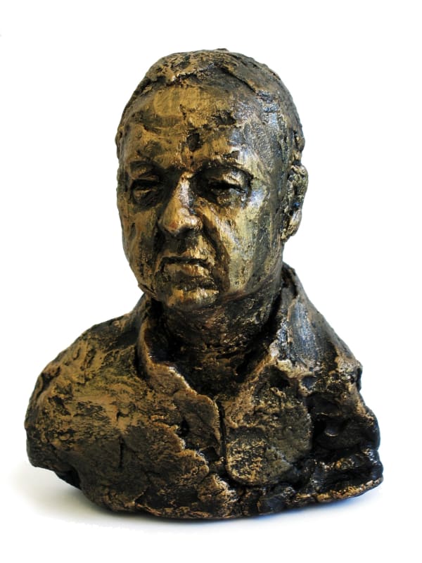 A textured bronze small bust titled Frank Minibust, depicting a middle-aged man with a solemn expression. The sculpture emphasizes the raw and expressive details of the face, with a rough, organic texture covering the head, neck, and partial upper torso. The patina combines golden and darker tones, adding depth and character to the piece. The bust conveys strength and introspection.