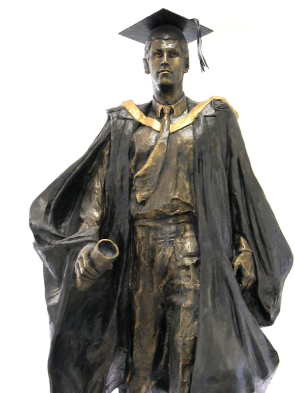 A bronze statue of a male graduate at Macquarie University, depicted walking confidently forward, wearing academic robes, a mortarboard, and holding a rolled-up diploma. His expression is determined, symbolizing achievement and progress.