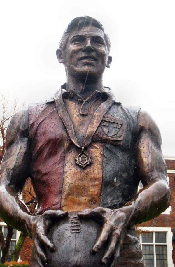 A close-up view of the Neil Roberts bronze statue, showcasing his confident facial expression. The polished surface highlights intricate details, including the medal around his neck and the texture of his uniform.