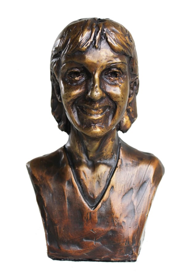 A bronze miniature bust of Lisa Mari, showcasing her smiling face with detailed features. The sculpture reflects a warm and loving expression, capturing her likeness in a heartfelt and artistic manner.