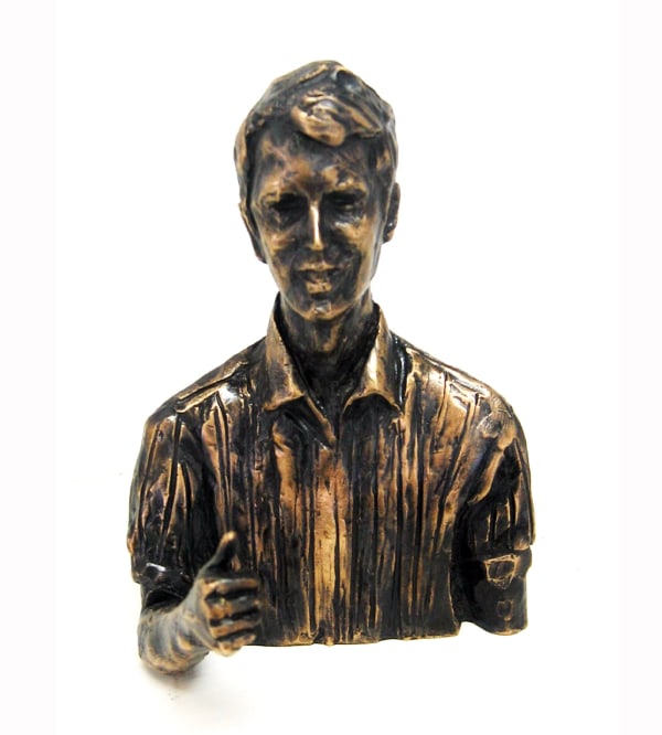 A bronze minibust of Alan Bailey, featuring a youthful and confident demeanor. He is depicted with short, neat hair and a slight smile, wearing a shirt with intricate vertical detailing and an open collar. The pose includes one hand raised, adding a sense of dynamism to the sculpture.
