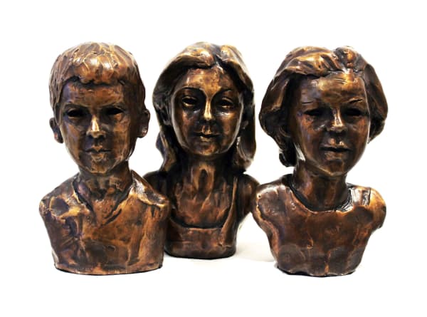 A trio of bronze minibusts depicting three siblings. The sculptures capture a young boy, a girl in the center, and another girl on the right. Each bust is crafted with detailed expressions and textured surfaces, highlighting their individual features while emphasizing familial unity. The central girl has long hair, while the girl on the right has shorter hair. The boy has a composed expression with short hair. Together, the busts create a touching representation of sibling connection and childhood.
