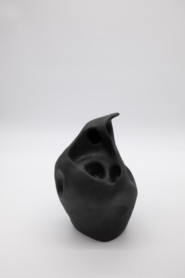 An abstract ceramic sculpture by Emily DiPalo in the shape of a black ghost. The top is pointed and there are random holes throughout.