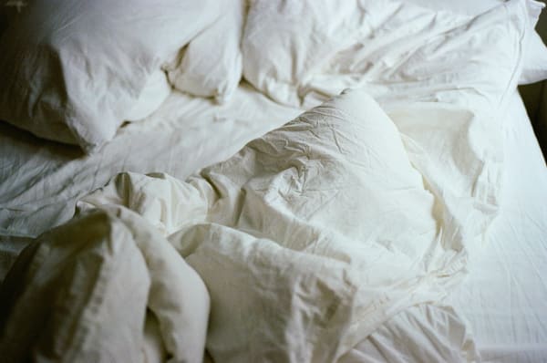 Photograph by Casey Joiner of unmade white bedsheets on an empty bed.