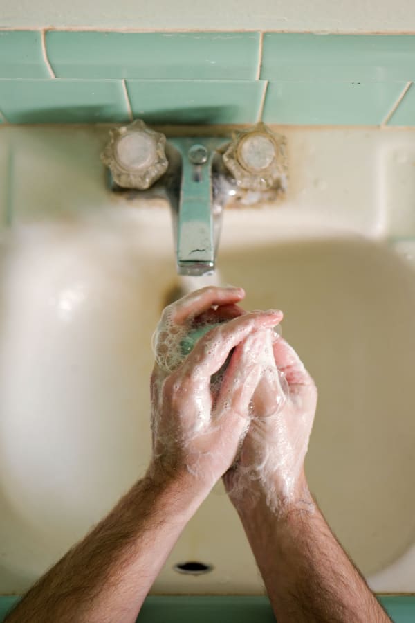 Photograph by Casey Joiner of a man washing his hands with bar soap from a top down angle over a white sink with turquoise tiled trimming.