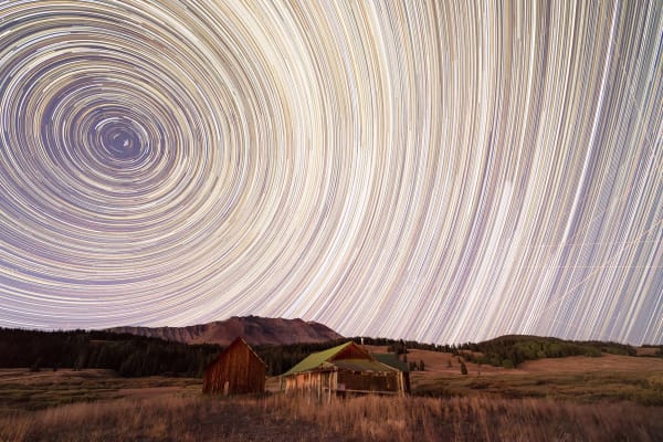 Photograph of a cabin in the mountains with a swirl of stars by slate gray gallery artist Ryan Bonneau