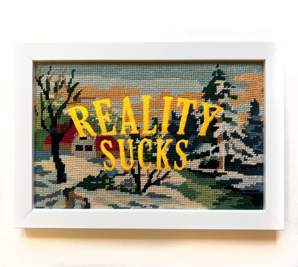 Embroidery on vintage needle-point reading "Reality Sucks"