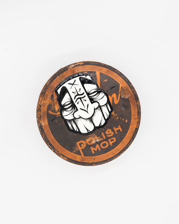 Circular metal tin with GATS character in black and white drawn on the top
