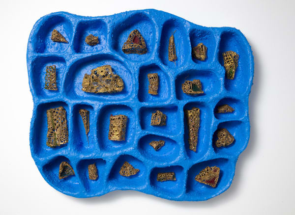 Bright blue tray type object with small sections each holding a small sculptural object