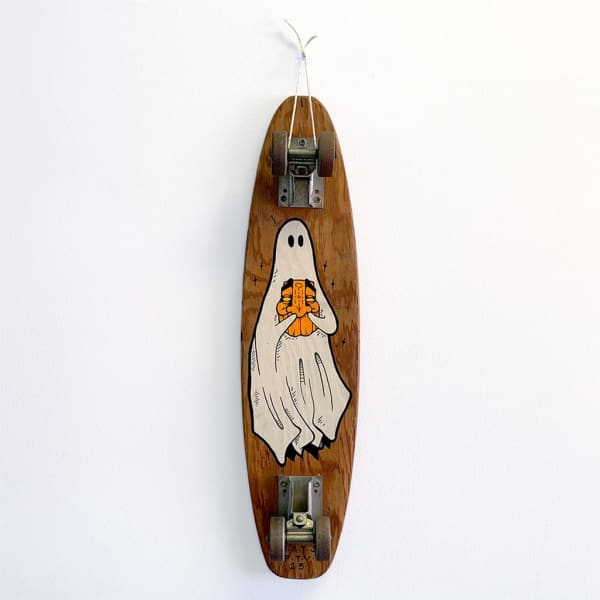 A vintage wood skateboard with a painting of a ghost holding an orange mask-like face.