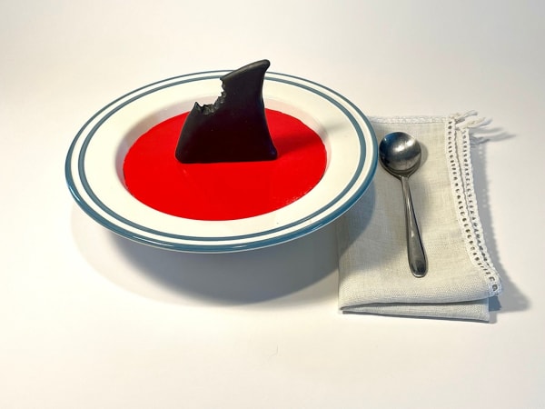 sculpture of a bowl of red soup with a shark fin in it