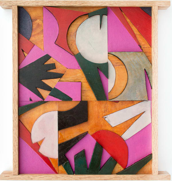 Abstract wooden collage with different shaped pieces of wood painted red, pink, dark green, black and white in a wooden frame.