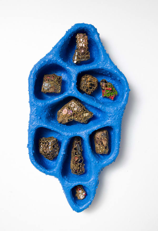 Bright blue tray type object with small sections each holding a small sculptural objects