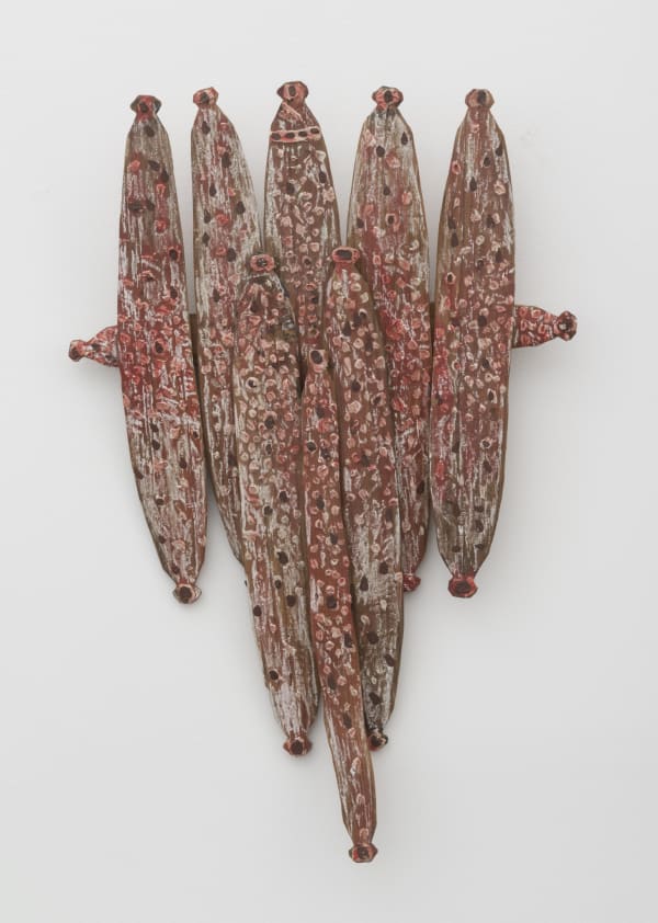 A wall sculpture made of seven pieces of red painted wood, similar to ears of corn, on one vertical piece