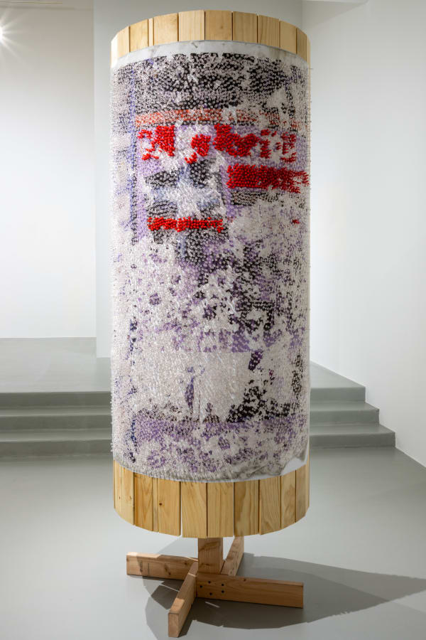 Round freestanding wood sculpture with an abstracted image adhered to the surface and obscured by thousands of clear push pins