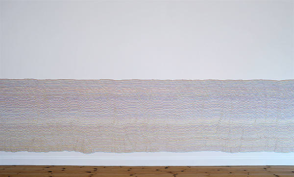 A white wall with many copied irregular lines in marker that go all the way from one end of the wall to the other, beginning at the middle of the wall and continuing to the floor