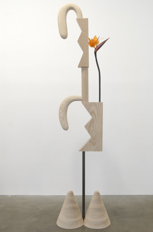 Carved wood abstraction in blonde wood, two cones as base attached to rod and wood carving with two long rabbit ear shapes, orange flower inserted into structure