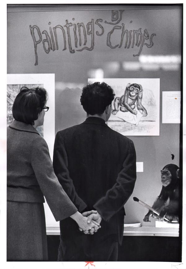 Black and white photograph of two people holding hands in front of Paintings by Chimps exhibition