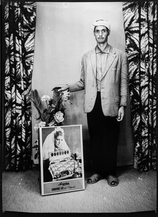 1960s black & white photograph of a man wearing a headscarf with a poster, in a photography studio