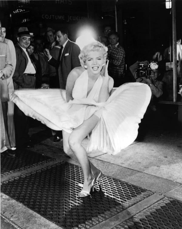 Marilyn Monroe on set in a white dress blown upward by the air of a New York City sewer grate, 1954