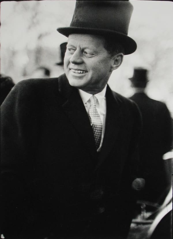 Black and white photograph of John F Kennedy in a top hat looking over his shoulder during inaugural festivities