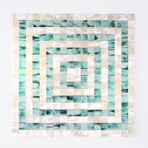 Sculpture composed of alternating green and beige iridescent concentric squares mounted on a white wall