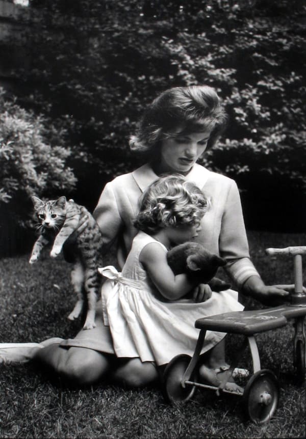 Black and white photograph of Jackie and Caroline Kennedy sitting in the grass with two kittens and a toy car
