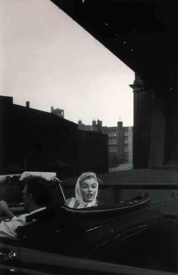 Black and white photograph of Marilyn Monroe and Arthur Miller driving under a bridge in a Thunderbird convertible