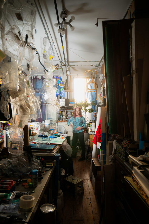 an artist, Vernita N'Cognita standing at the end of a hallway in a loft setting filled with plastic containers and other materials