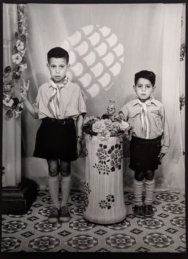 1960s black & white photograph of two children in school uniforms, in a photography studio