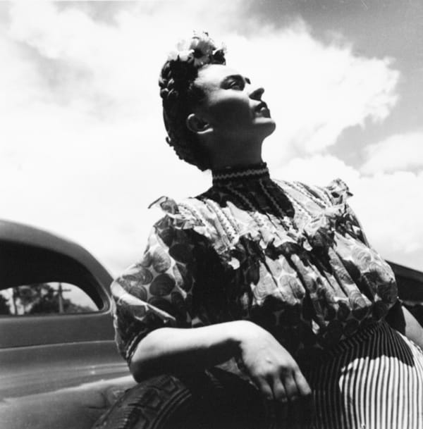 Black and white photograph of Frida Kahlo leaning against a car and looking up