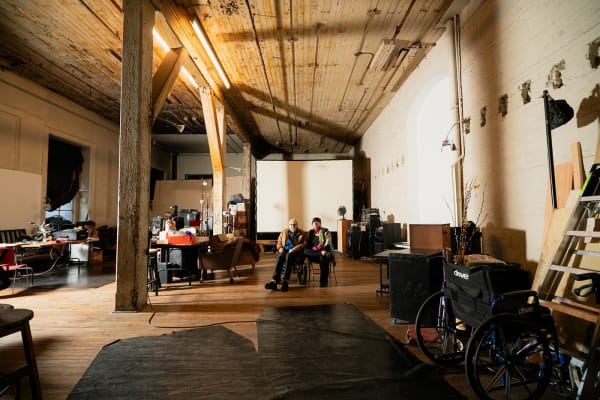Two artists, Phillips Niblock and Katherine Liberovskaya sitting in the center of a large industrial loft with work tables and furniture