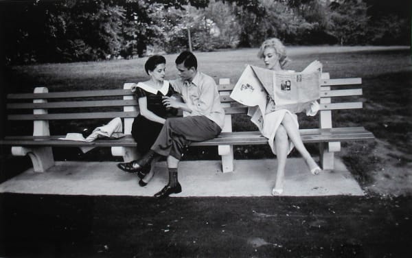 Marilyn Monroe in white dress reading a newspaper on a Central Park bench next to a couple in New York City, 1956
