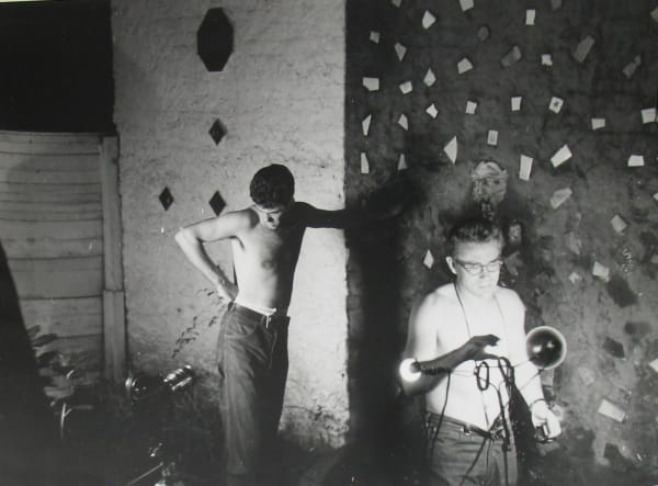 Black and white photograph of James Dean and another figure, both shirtless, working with a lamp in a backyard setting