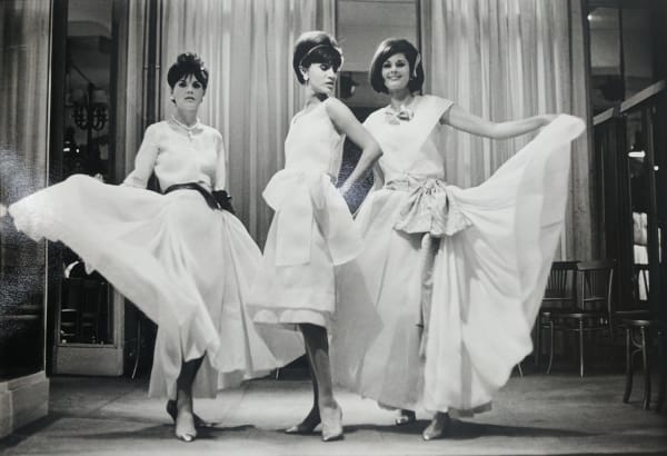 Black and white photograph of three models wearing white Chanel dresses of different lengths and styles