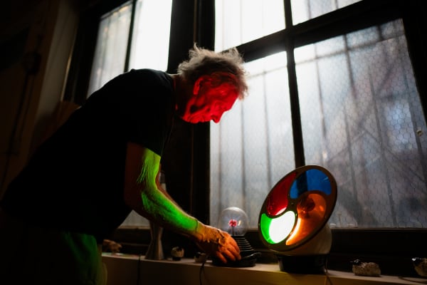 Artist Gerald Marks' face is illuminated by red light as he looks into a color