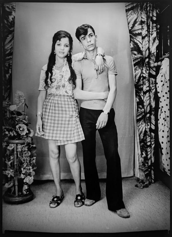 1960s black and white photograph of a couple standing with their arms wrapped around each other in a photography studio