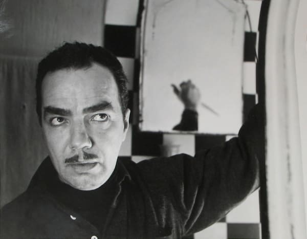 Black and white photograph of Roy Shatt holding up one arm in front of a checkerboard tiled wall and mirror, which reveals that he is holding a knife