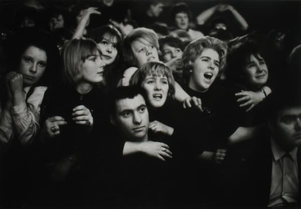 Black and white photograph of a large crowd of women screaming and pushing to the front of the stage at a Beatles show, portraying “Beatlemania”