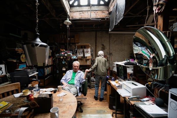 Two artists, Ken and Flo Jacobs in a loft setting filled with artworks, books, and tools