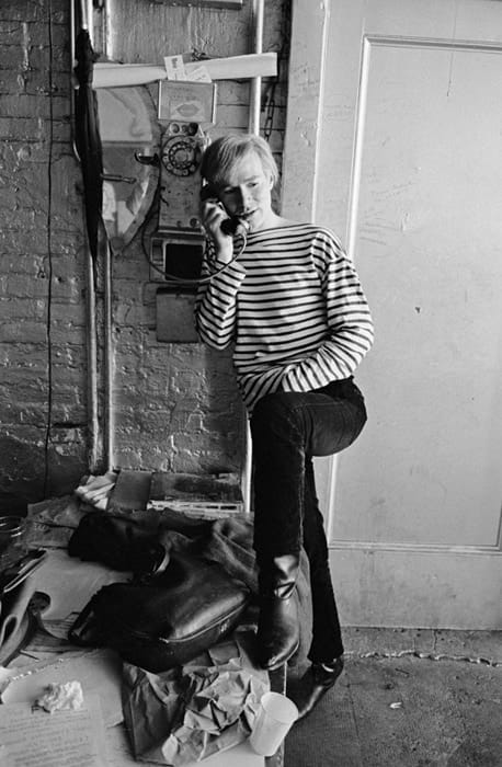 Black and white photograph of Andy Warhol speaking on a rotary dial telephone
