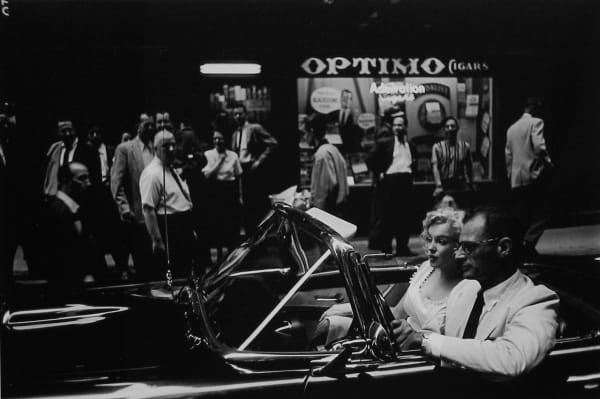 Marilyn Monroe and Arthur Miller drive by Optimo Cigars storefront and crowd in New York City, 1956